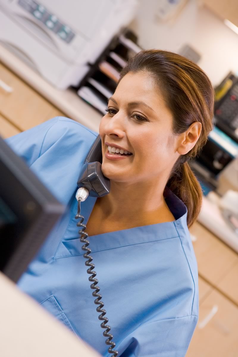 Nurse smiling on the phone at a hospital reception area. 