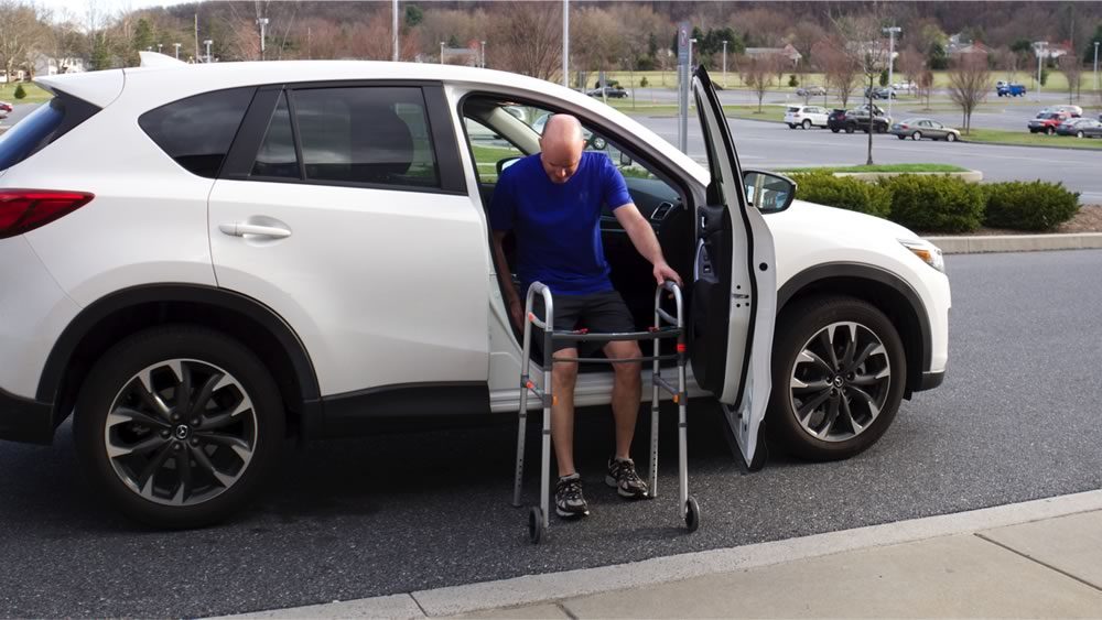 Man getting into a vehicle using a walker for support. 
