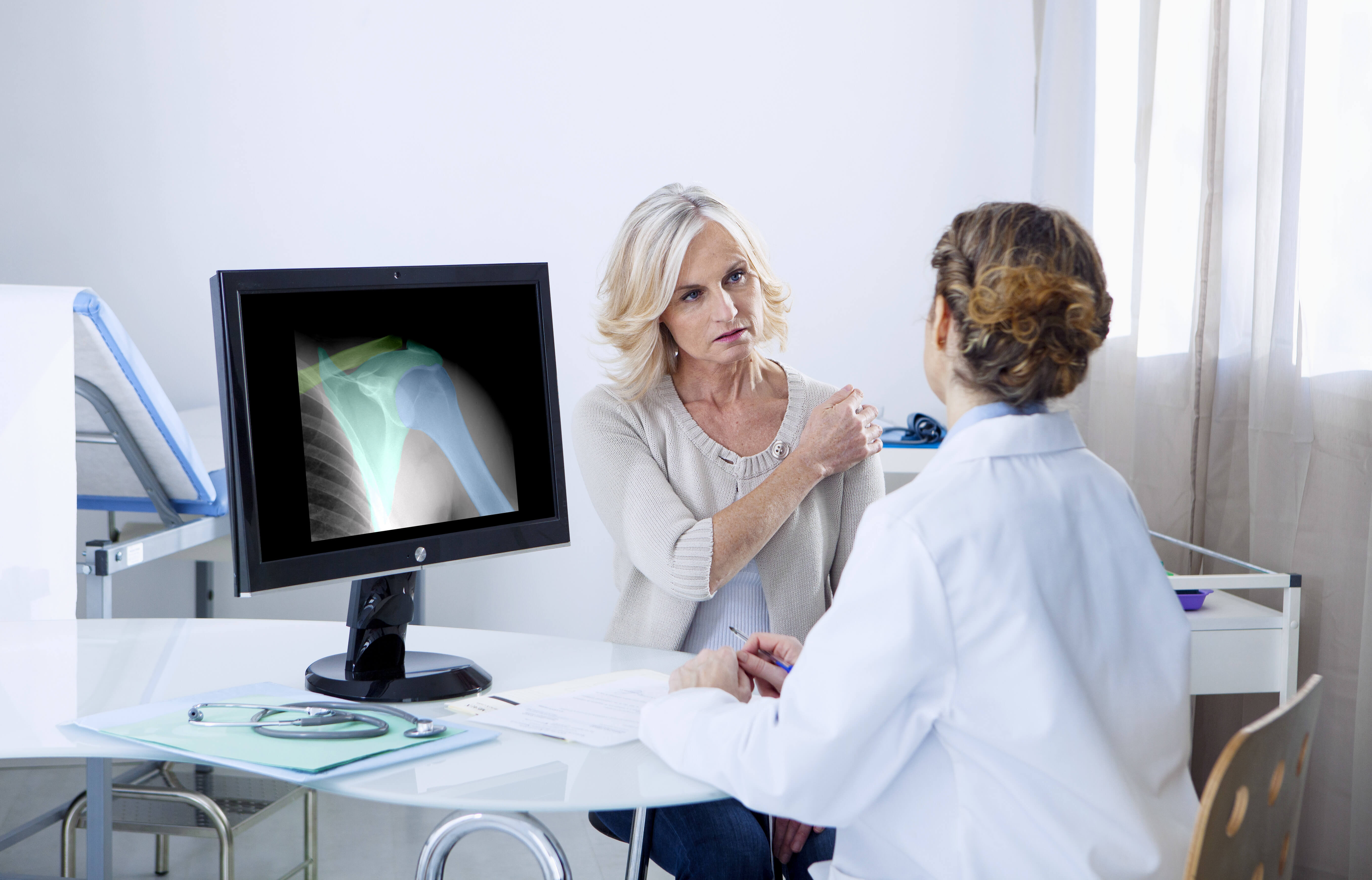 Female patient consulting with female doctor next to computer screen with x-ray displayed.