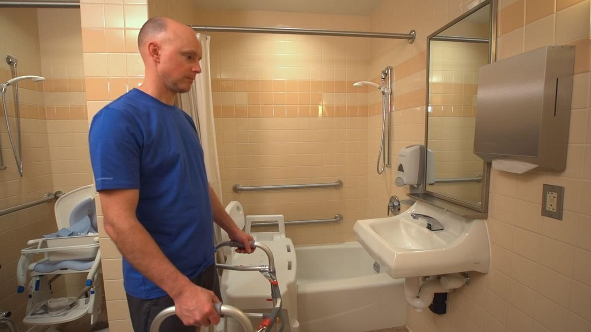 man in bathroom with walker, grab bars and shower chair available 
